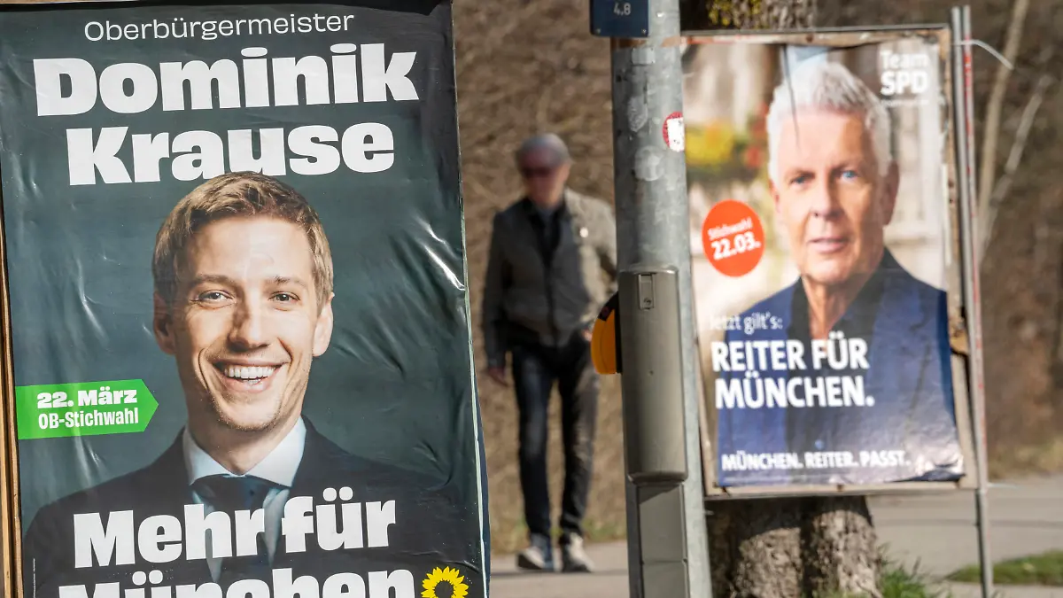 Deutschland, München, 19. März 2026, Wahlplakate Dominik Krause und Dieter Reiter, beide stehen in der Stichwahl um das Amt des Münchner Oberbürgermeisters am 22. März , Dominik Krause, Die Grünen, Zweiter Bürgermeister der Stadt München, Wahlslogan Mehr für München, OB-Kandidat der Münchner Grünen, Oberbürgermeister Dieter Reiter, SPD, Wahlslogan Reiter für München, Münchner Kommunalwahlkampf, Plakate an der Putzbrunner Straße, Passant, Politiker, Politik, Wahlkampf, Bayern