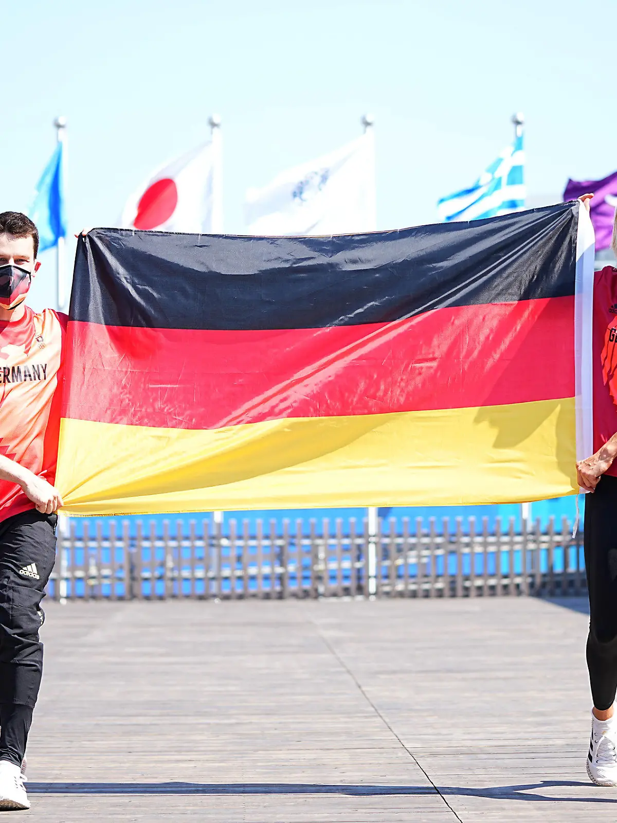 22.07.2021, Japan, Tokio: Wasserspringer Patrick Hausding (l) und Beachvolleyballspielerin Laura Ludwig halten eine Deutschlandfahne vor der Pressekonferenz vom Deutschen Olympischen Sportbund (DOSB) zur Vorstellung des Fahnenträger-Duos vom Team Deutschland für die Eröffnungsfeier der Olympischen Spiele 2020 Tokio. Laura Ludwig und Patrick Hausding werden das deutsche Olympia-Team bei der Eröffnungszeremonie am Freitag (23.07.2012) als Fahnenträger ins Kasumigaoka National Stadium in Tokio führen. Foto: Michael Kappeler/dpa +++ dpa-Bildfunk +++