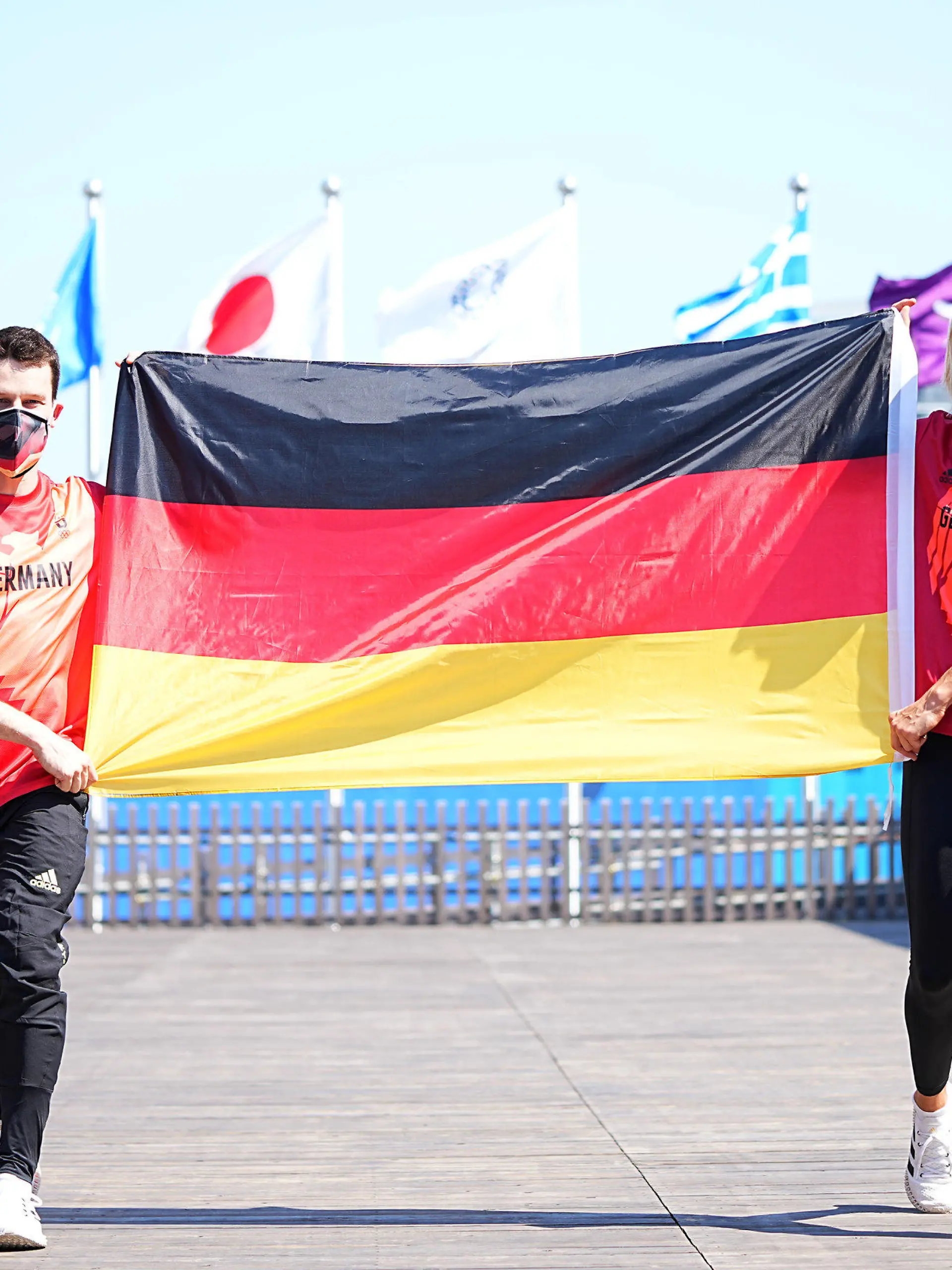 22.07.2021, Japan, Tokio: Wasserspringer Patrick Hausding (l) und Beachvolleyballspielerin Laura Ludwig halten eine Deutschlandfahne vor der Pressekonferenz vom Deutschen Olympischen Sportbund (DOSB) zur Vorstellung des Fahnenträger-Duos vom Team Deutschland für die Eröffnungsfeier der Olympischen Spiele 2020 Tokio. Laura Ludwig und Patrick Hausding werden das deutsche Olympia-Team bei der Eröffnungszeremonie am Freitag (23.07.2012) als Fahnenträger ins Kasumigaoka National Stadium in Tokio führen. Foto: Michael Kappeler/dpa +++ dpa-Bildfunk +++