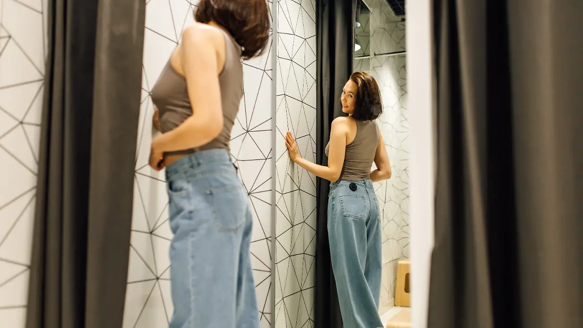 Frau probiert blaue Jeans in Umkleidekabine an.