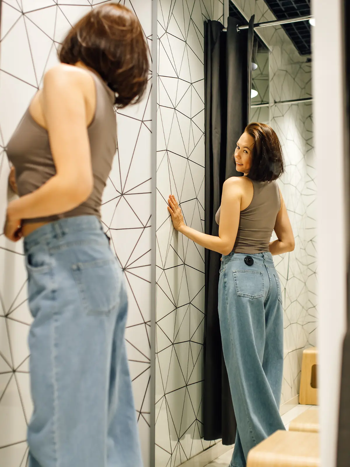 Frau probiert blaue Jeans in Umkleidekabine an. 