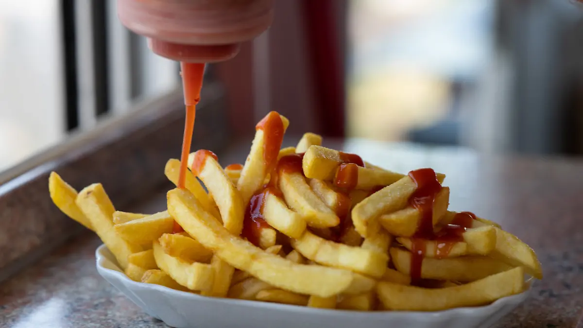 Ketchup wird auf Pommes verteilt.