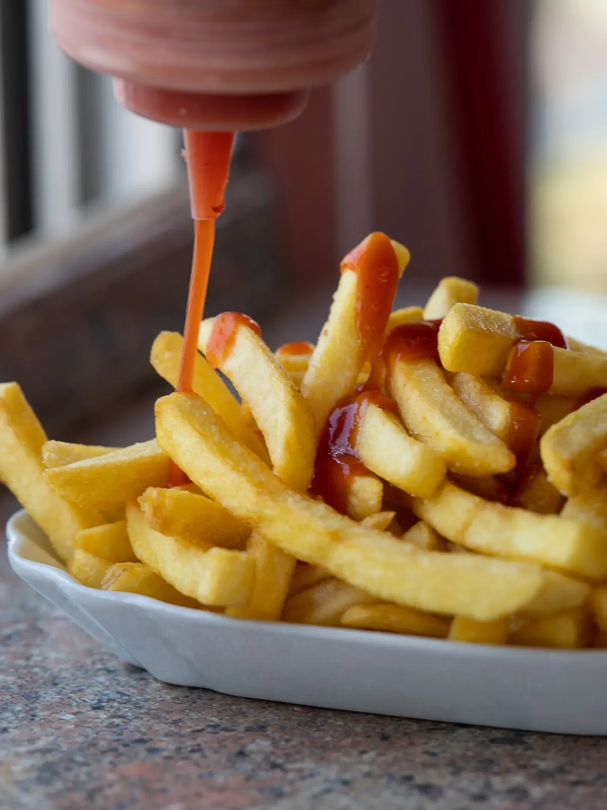 Ketchup wird auf Pommes verteilt.