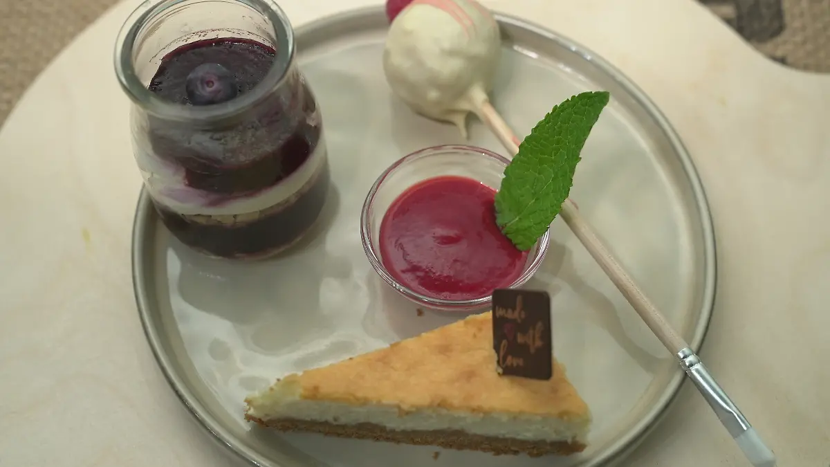 Das perfekte Dinner: Teller, auf dem das Dessert angerichtet ist: weißer Cakepop, Käsekuchen im Glas, Zitronen-Käsekuchen, Fruchtsauce