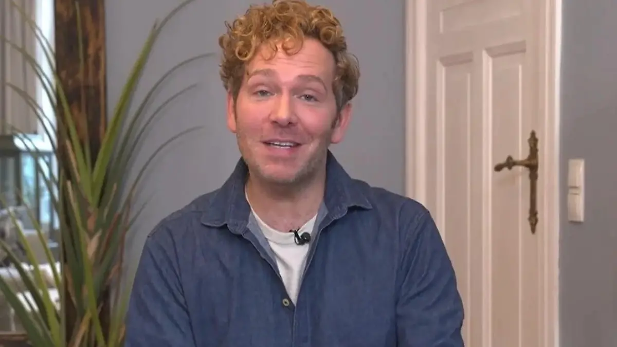 Das perfekte Dinner: Junger Mann mit kurzer Lockenfrisur, blauem Hemd und beigefarbener Hose