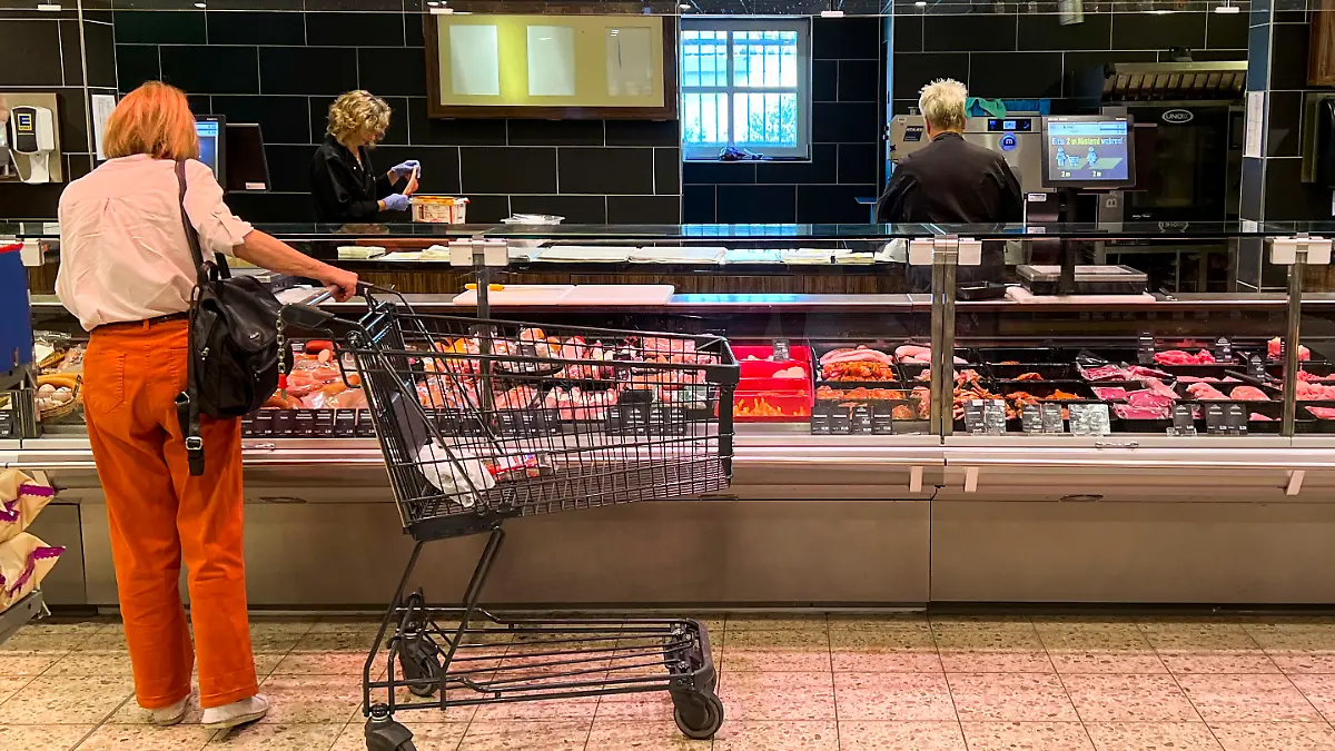 Symbolfoto-0916 Lebensmittel - Fleischtheke Kundin steht an einer mit Blick auf eine Fleischtheke Kuehltheke mit Auswahl frischer Fleisch und Wurstwaren Edeka Lebensmittel Abteilung im Supermarkt an der Bedintheke Metzgertheke mit Fleisch und Wurst