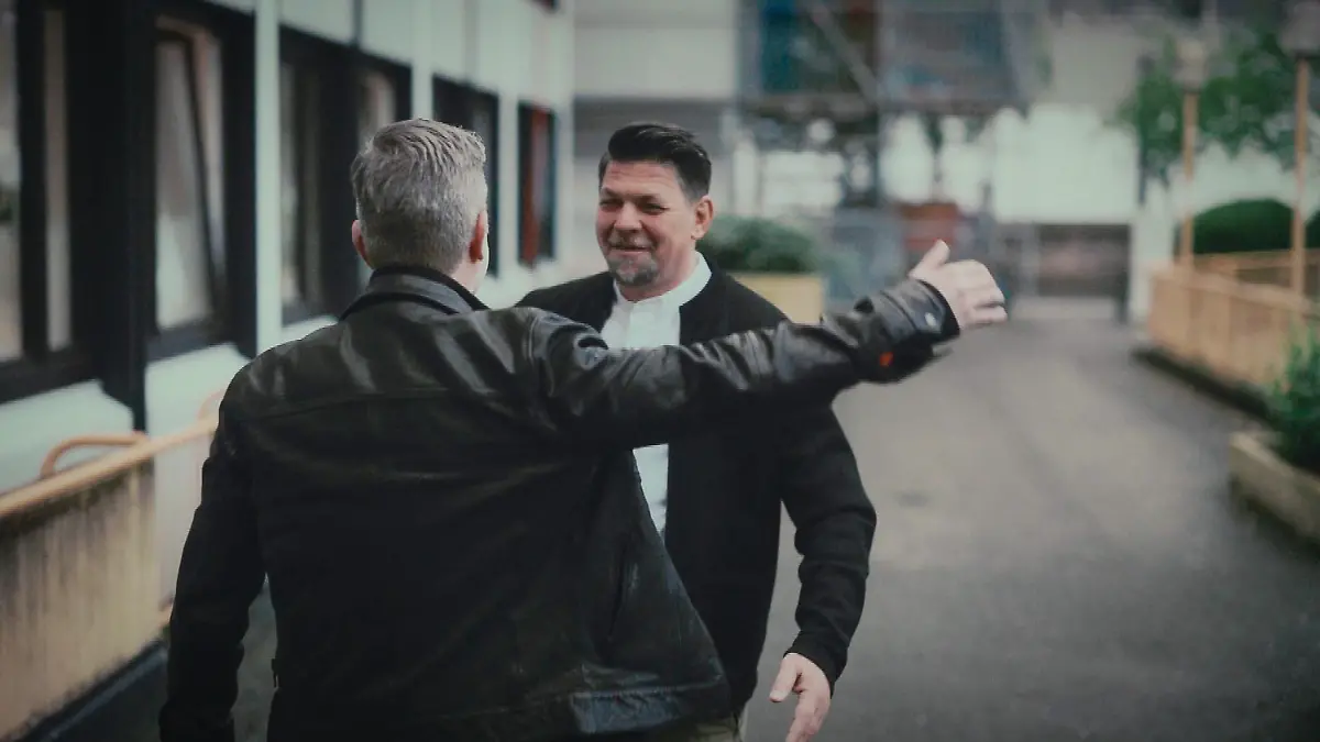 Herbstresidenz – Ein Jahr danach: Schauspieler André Dietz und Tim Mälzer gehen auf der Straße aufeinander zu, um sich zu umarmen