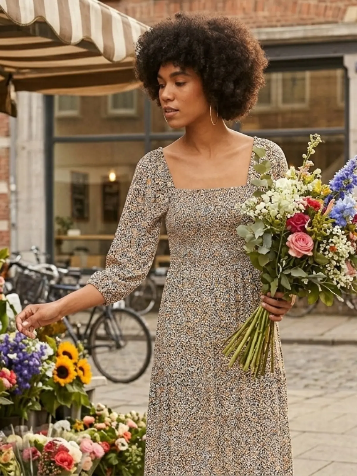 Frau trägt ein Kleid mit Blumenmuster und schaut sich Blumen an bei einem Floristen.