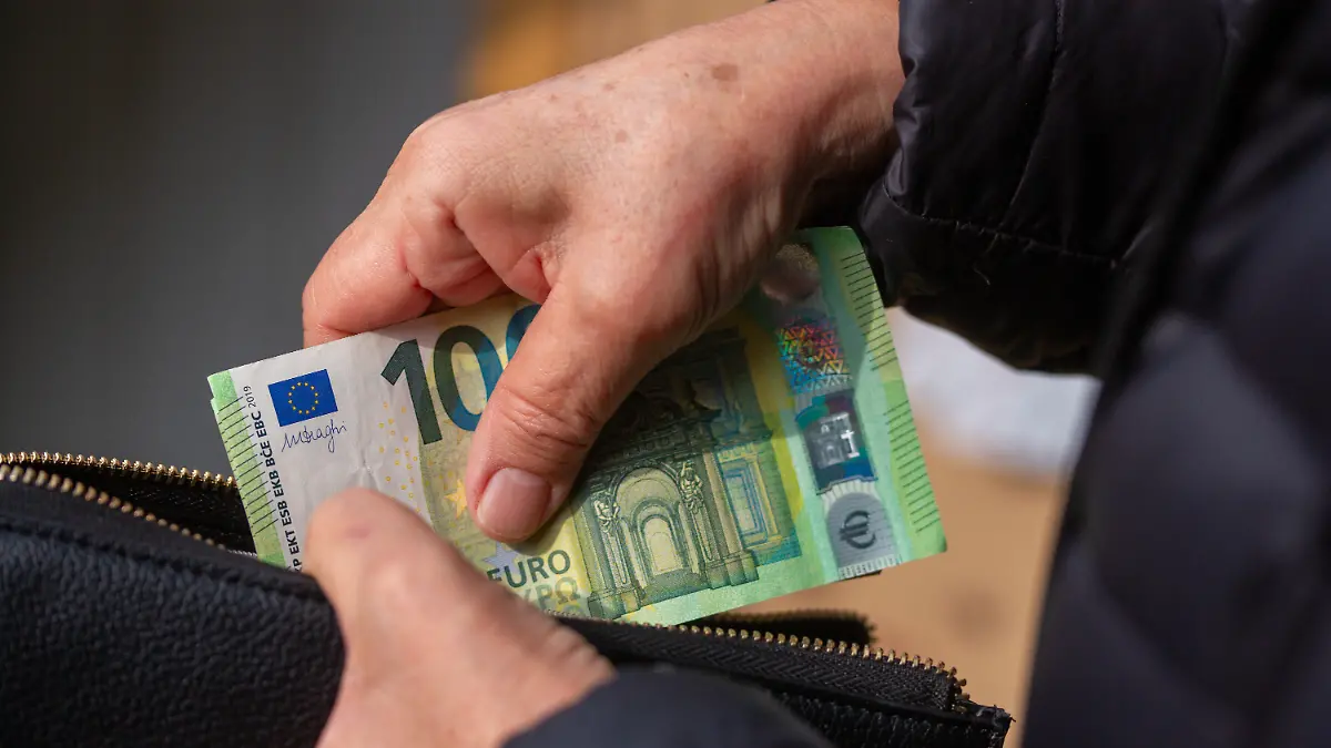 Eine Seniorin steckt Euro-Banknoten in eine Geldbörse.