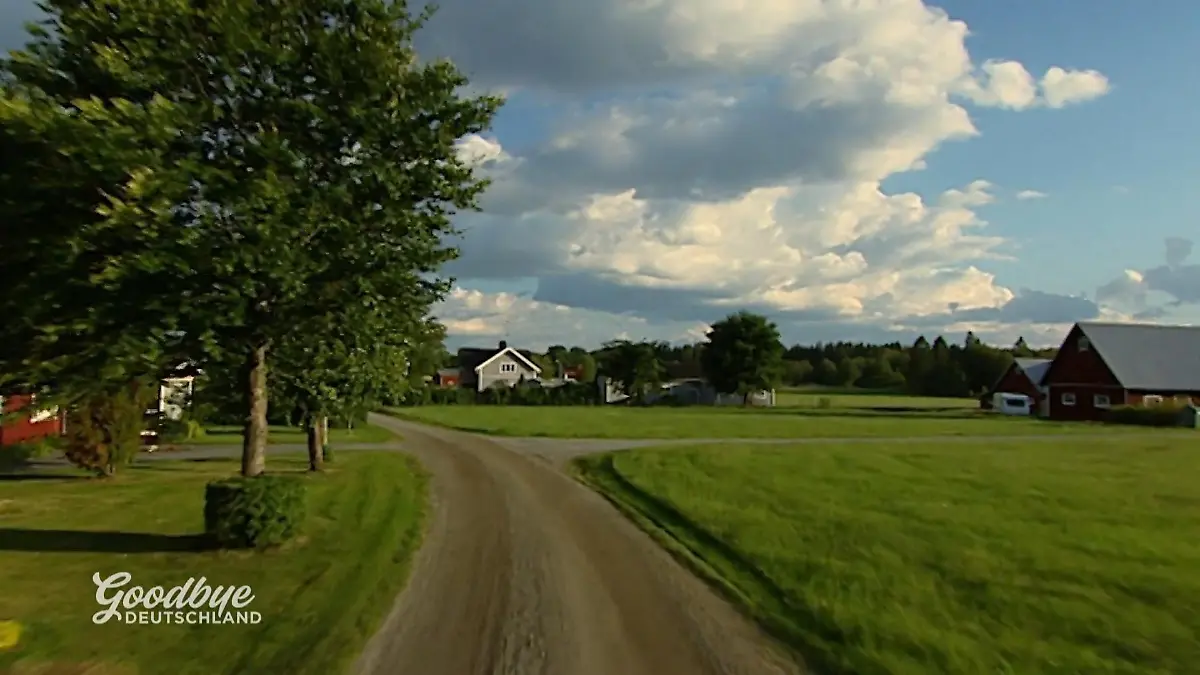 Goodbye Deutschland: Ein schwedisches Holzhaus inmitten einer grünen flachen Landschaft mit Gras und Bäumen
