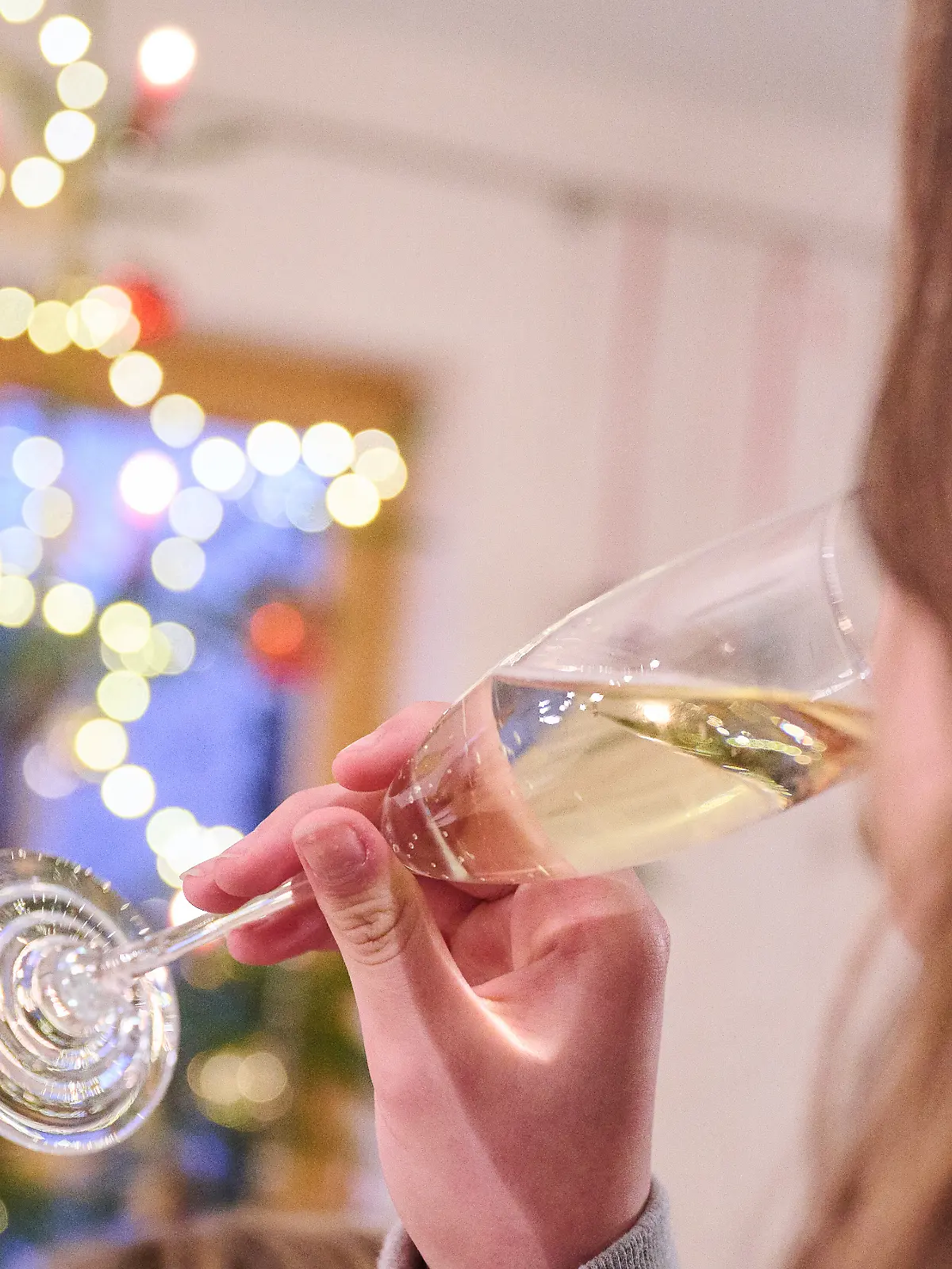 Ein Teenager trinkt ein Glas Sekt, während ein Weihnachtsbaum im Hintergrund leuchtet. +++ dpa-Bildfunk +++