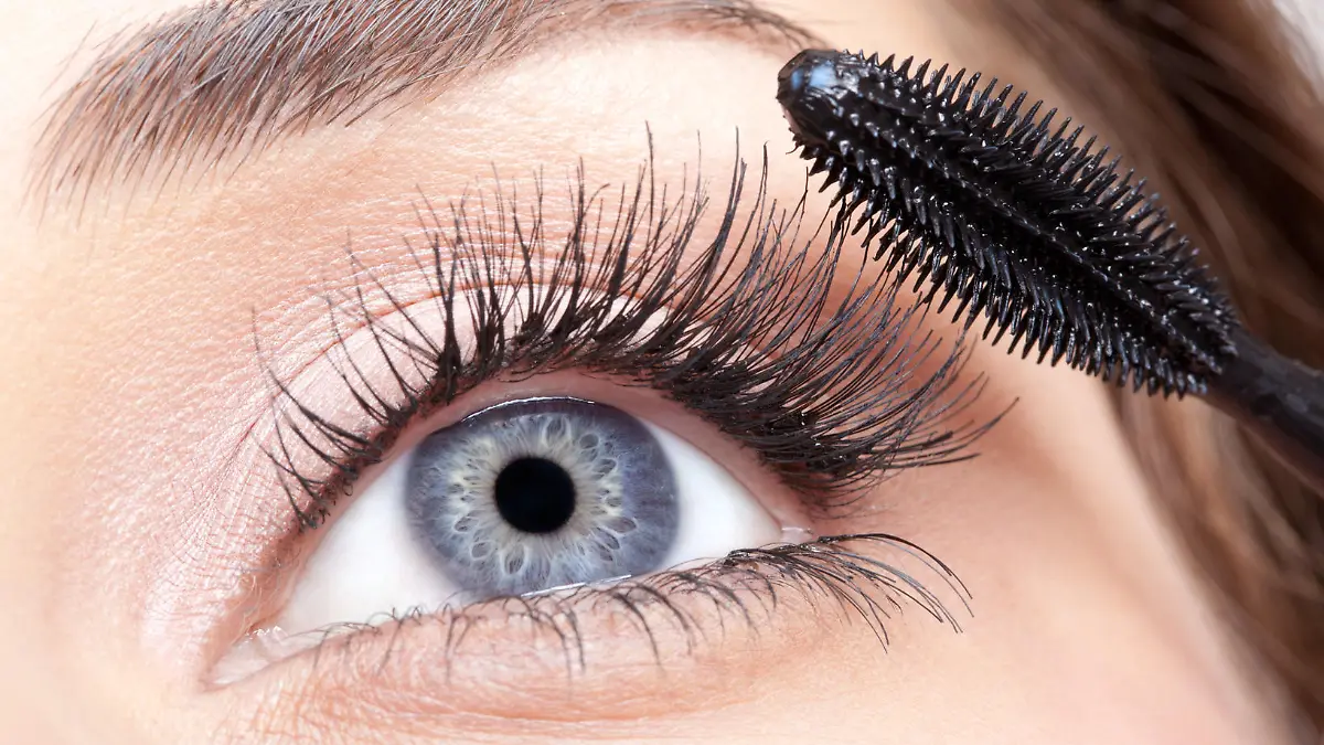 Young beautiful woman applying mascara makeup on eyes by brush