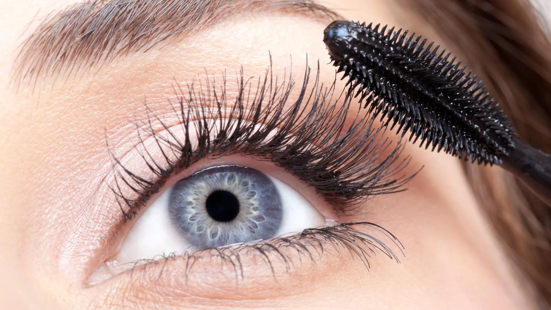Young beautiful woman applying mascara makeup on eyes by brush