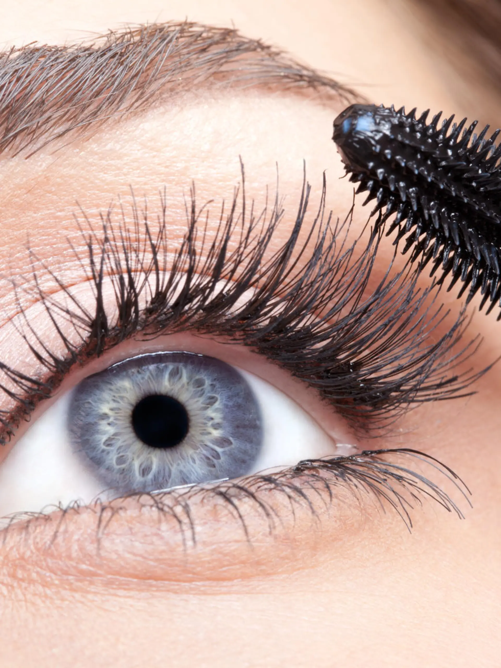 Young beautiful woman applying mascara makeup on eyes by brush