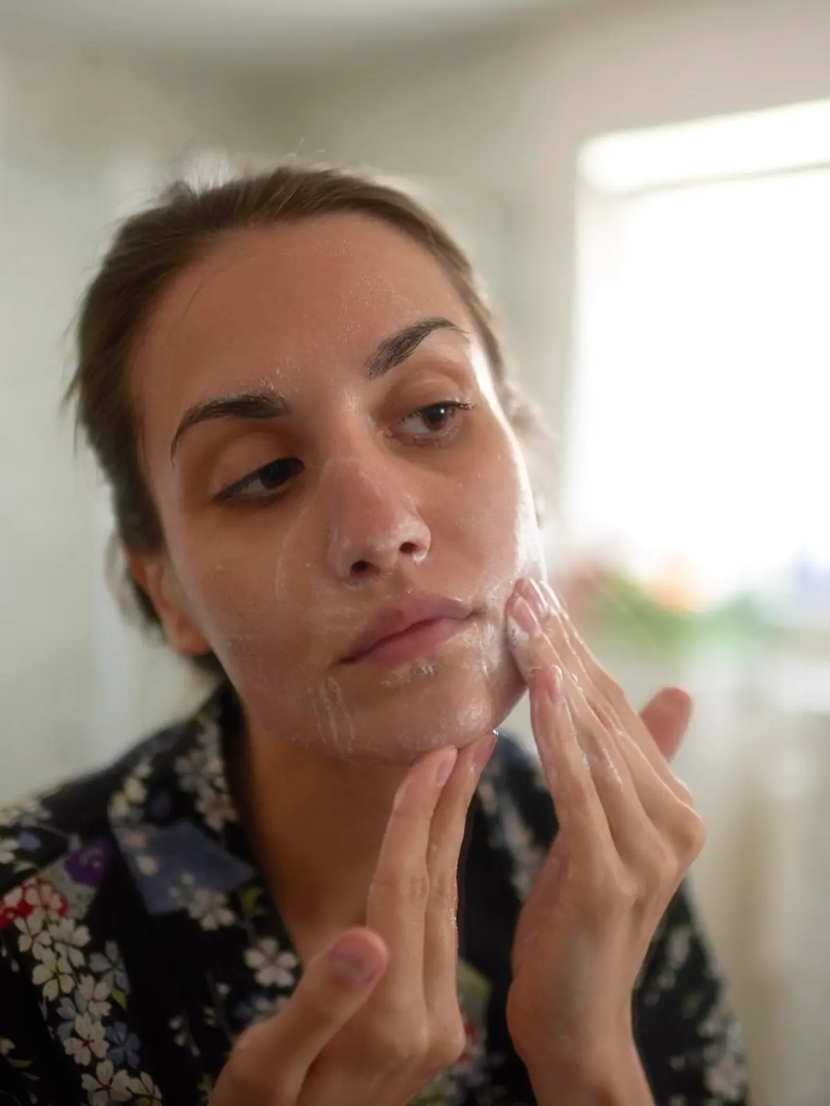 Frau im Badezimmer schmiert sich Creme ins Gesicht