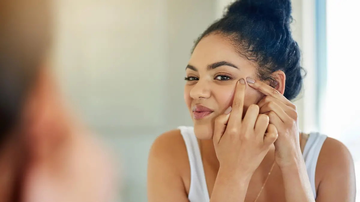 Shot of a young woman squeezing a pimple in front of the bathroom mirror