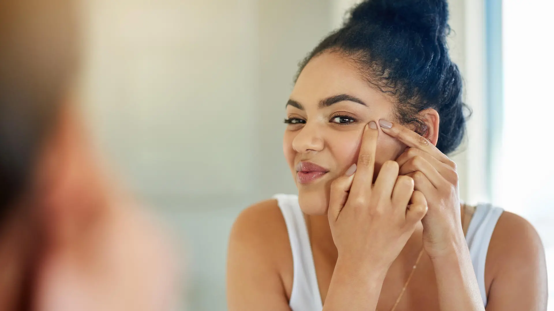 Shot of a young woman squeezing a pimple in front of the bathroom mirror