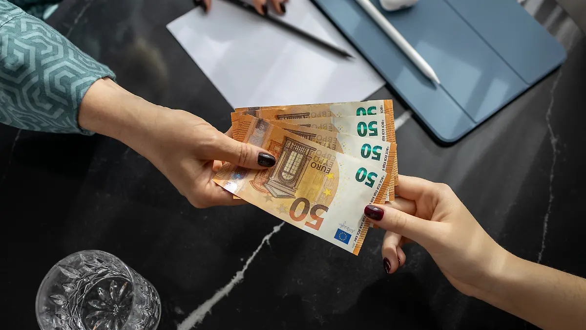 Nahaufnahme der Hände: Eine Frau gibt einer anderen Frau vier 50-Euro-Scheine.