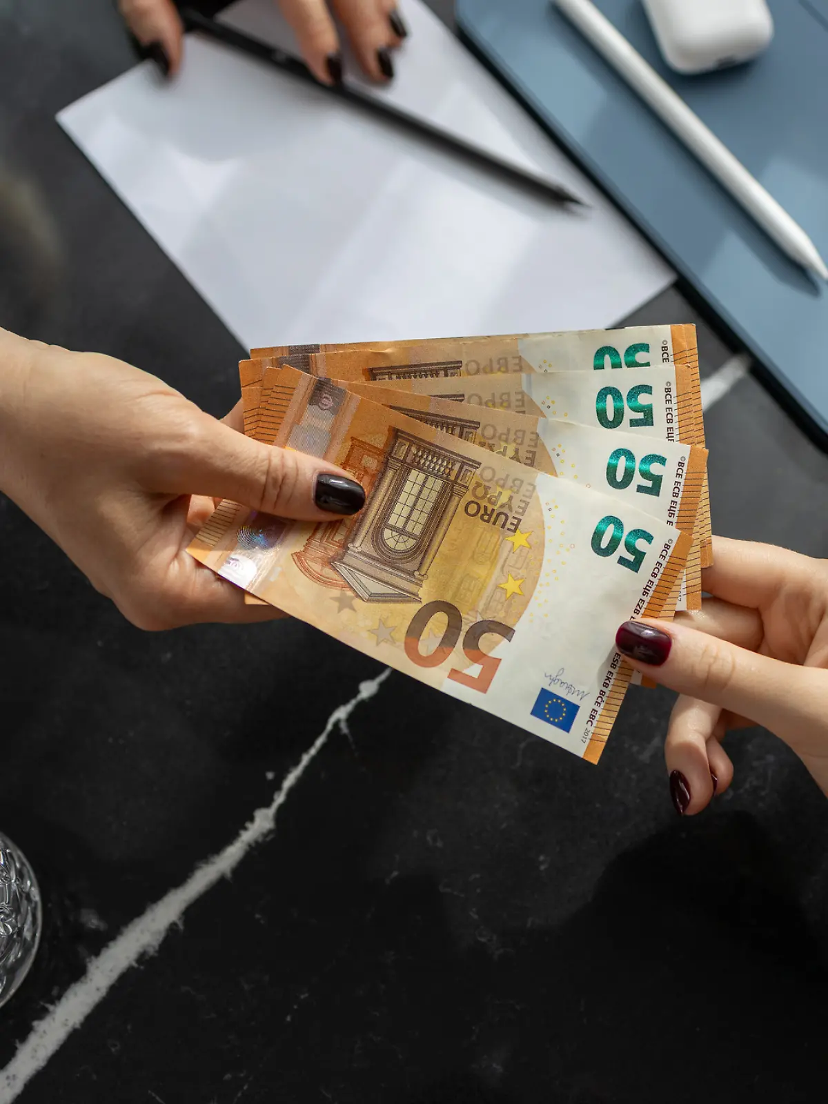 Nahaufnahme der Hände: Eine Frau gibt einer anderen Frau vier 50-Euro-Scheine.