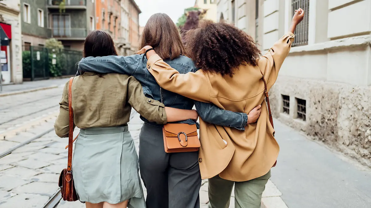 Drei Freundinnen sind von hinten zu sehen, wie sie Arm in Arm eine Straße entlanggehen.