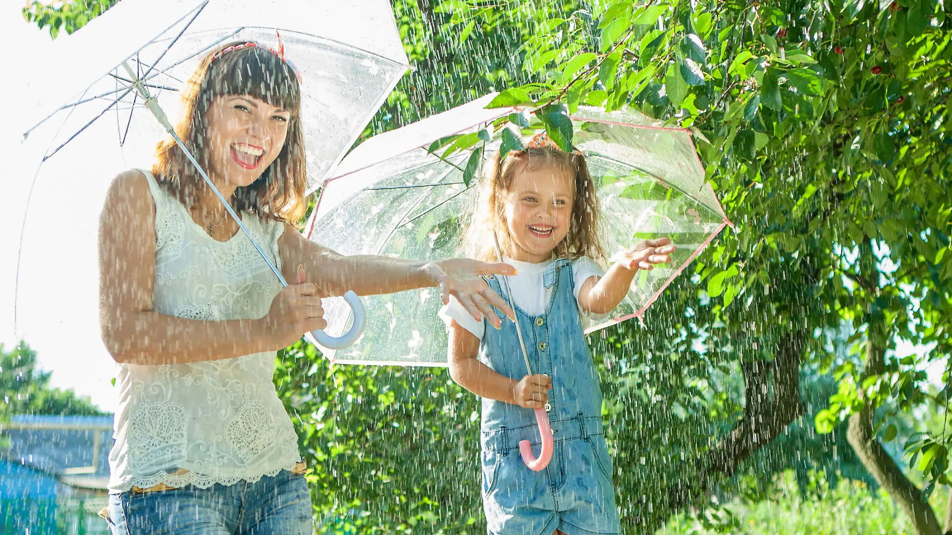 Happy family in the summer sunny rain. Funny Mother and daughter playing outdoors hot day with umbrella. Joyful emotions