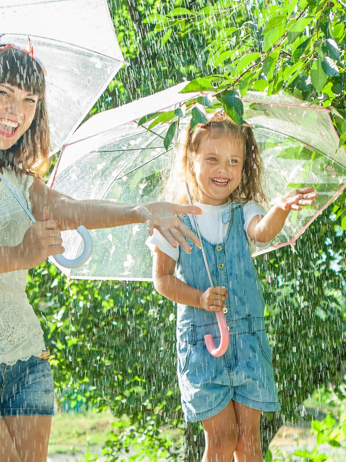 Happy family  in the summer sunny rain. Funny Mother and daughter playing outdoors hot day with umbrella. Joyful emotions