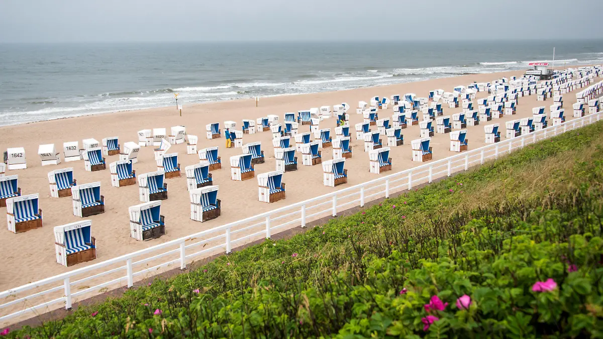 20.06.2021, Schleswig-Holstein, Westerland: Im Regen richtet ein Mann auf der Nordseeinsel Sylt am menschenleeren Strand Strandkörbe aus. Foto: Daniel Bockwoldt/dpa +++ dpa-Bildfunk +++