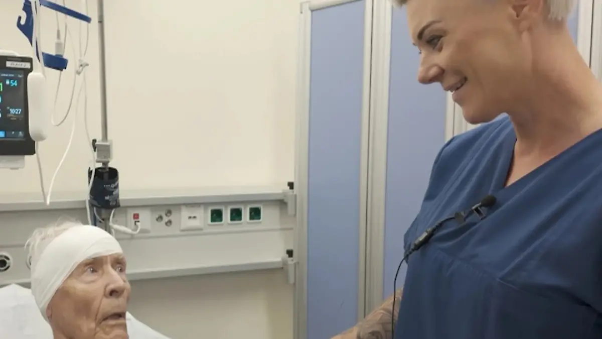 Doc Caro am Bett eines männlichen Patienten mit verbundenem Kopf