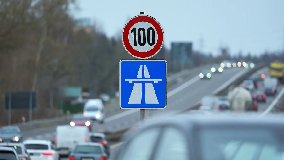 Ein Schild am Fahrbahnrand der Autobahn A 114 zeigt die Geschwindigkeitsbegrenzung auf Tempo 100 und das Symbol für den Beginn der Autobahn an. 