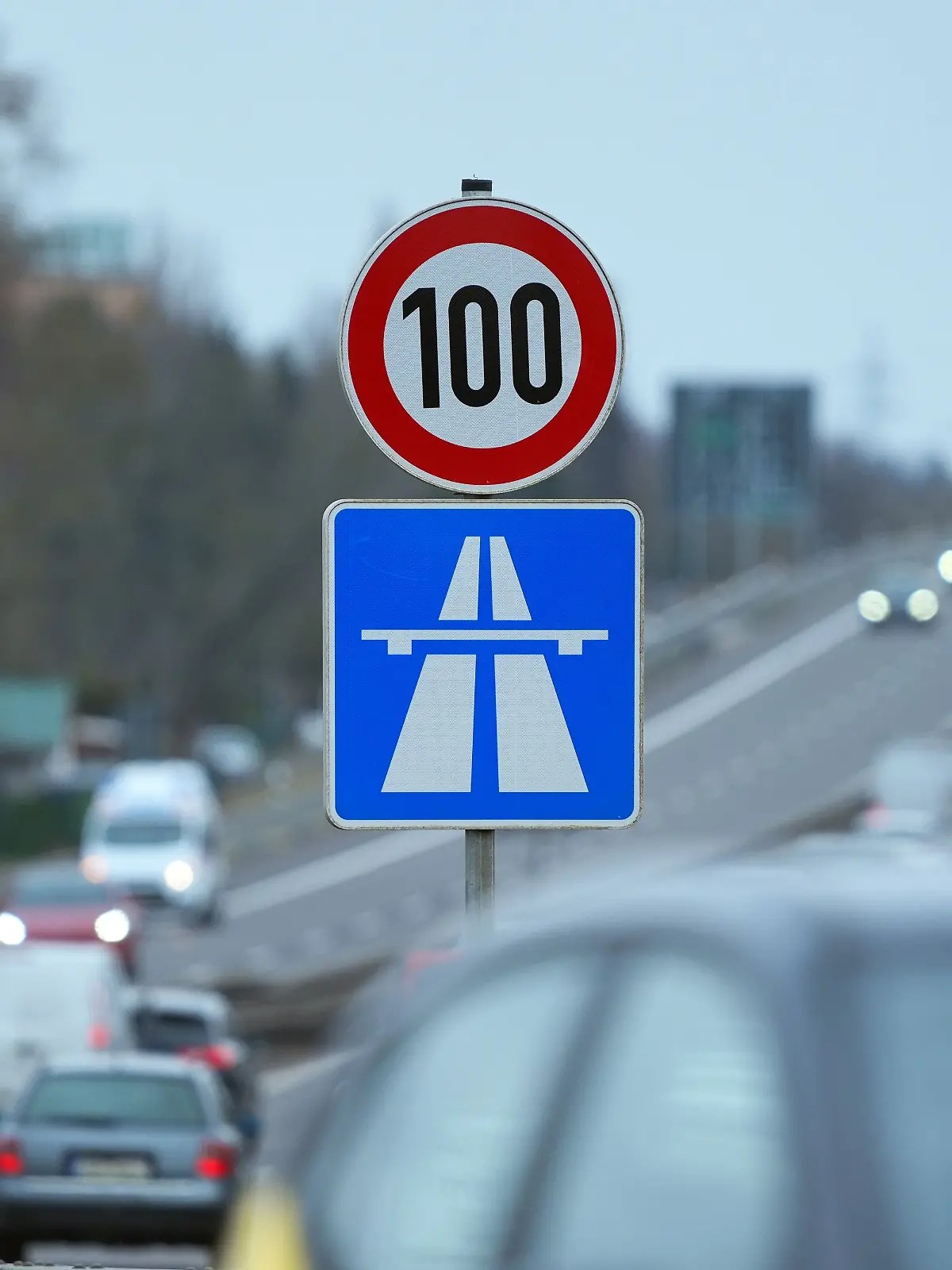 Ein Schild am Fahrbahnrand der Autobahn A 114 zeigt die Geschwindigkeitsbegrenzung auf Tempo 100 und das Symbol für den Beginn der Autobahn an. 
