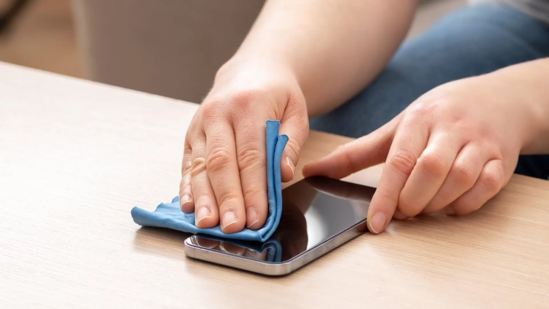 Person reinigt Handy-Display vorsichtig mit einem Brillentuch, das Kratzern vorbeugt.
