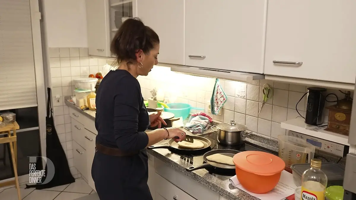 Hülya steht am Herd, vor ihr zwei Pfannen mit Teigfladen. 