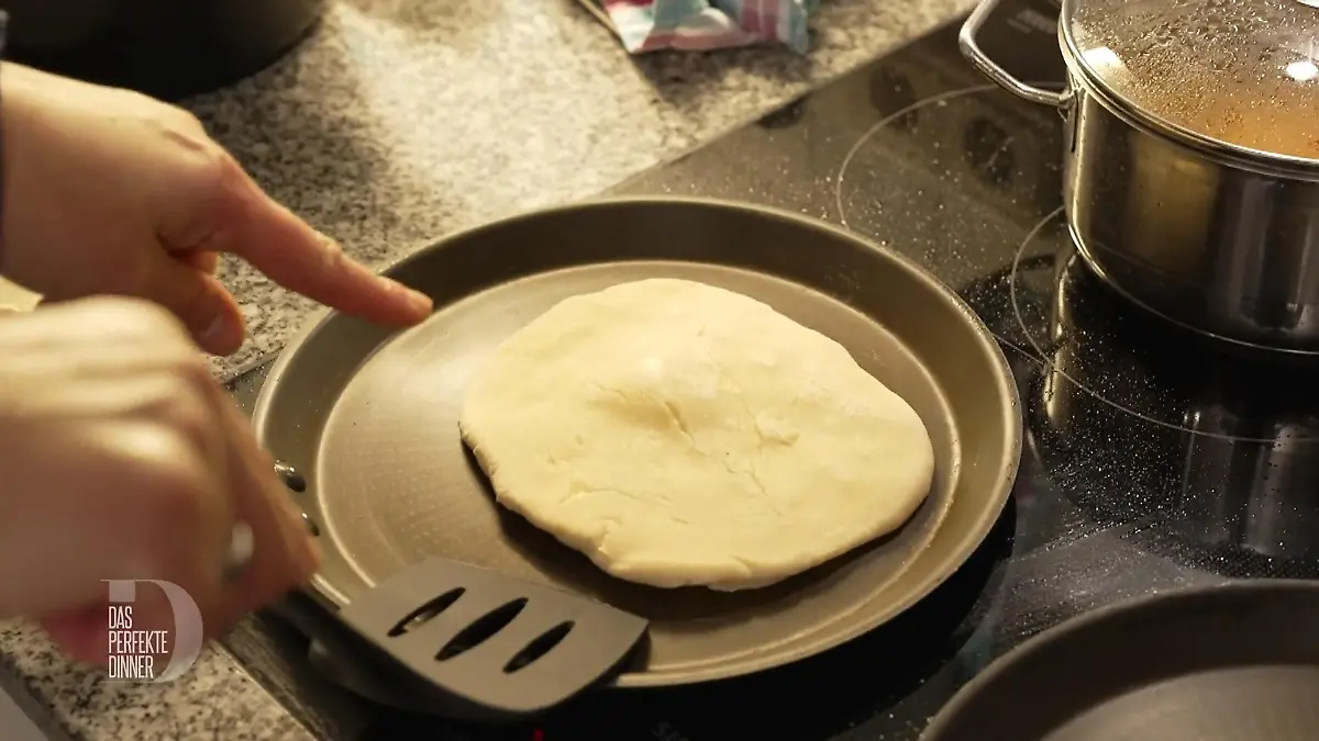 Ein Teigfladen in der Pfanne, bei dem sich die Mitte leicht wölbt.