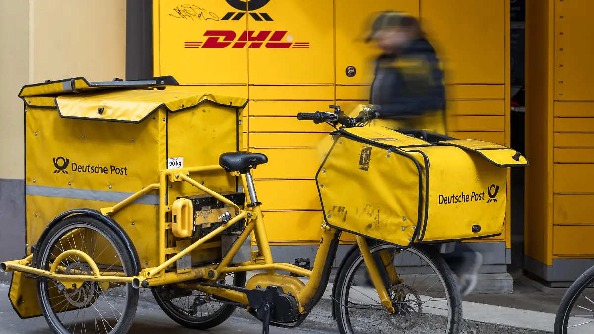 Ein Zustellfahrrad der Deutschen Post steht bereit, während ein Postbote Sendungen zustellt und transportiert. Die Nutzung von Lastenrädern ermöglicht flexible und nachhaltige Zustellung im urbanen Raum.