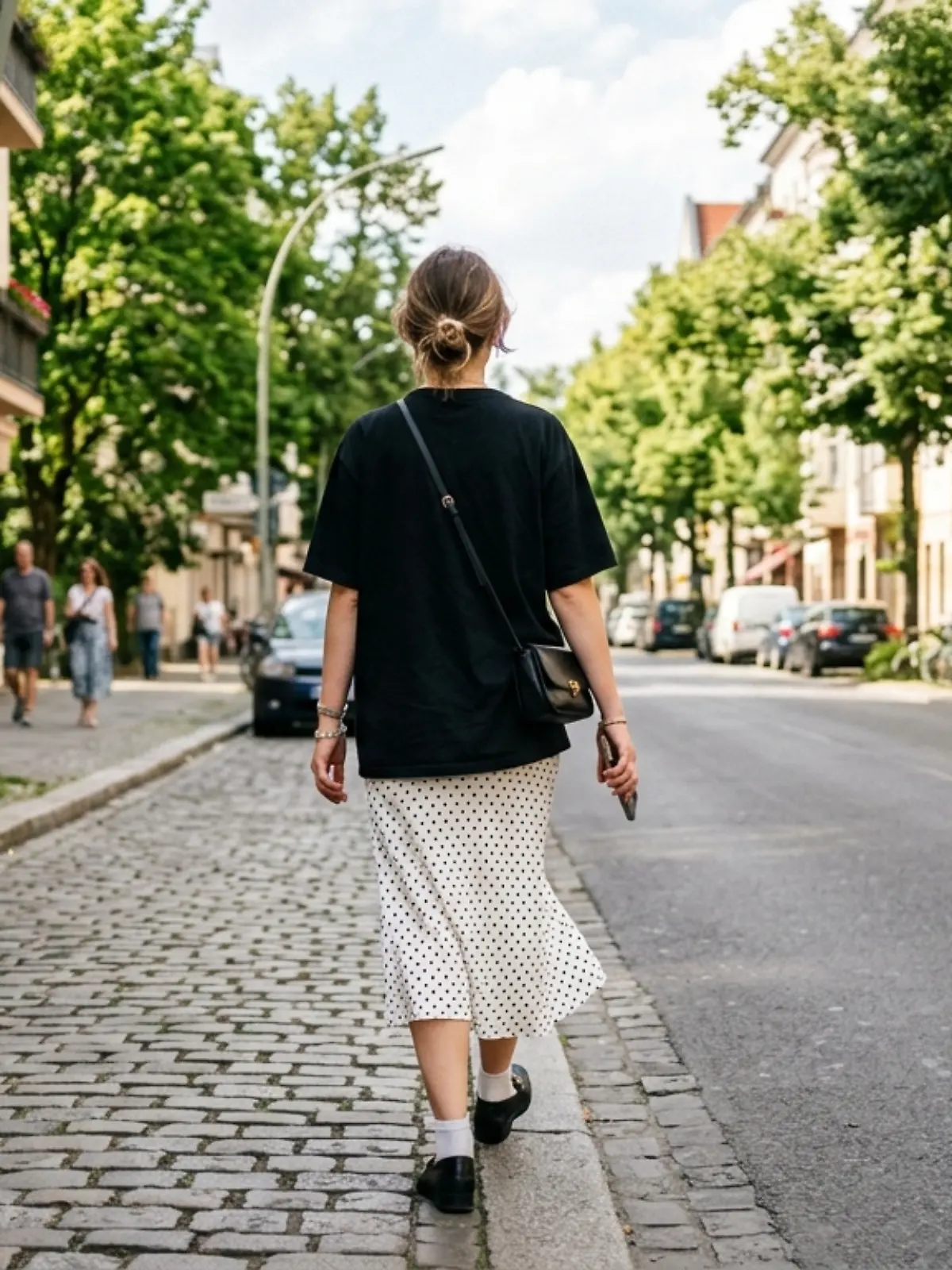 Frau in Punktemuster-Rock und schwarzem T-Shirt läuft auf einer Straße.