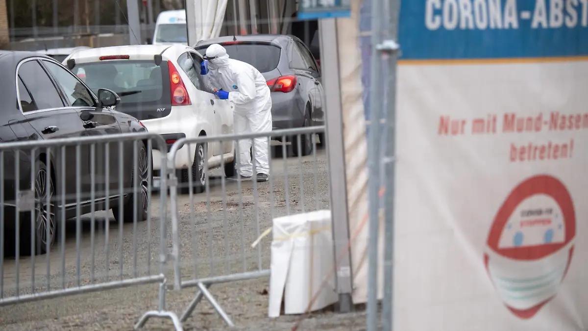 Mitarbeiter in Schutzkleidung stehen im Corona-Testzentrum auf dem Gelände des «Corona-Abstrichzentrum» der Universitätsmedizin Greifswald (UMG) an einem Auto. Nach Angaben eines UMG-Sprechers steigt derzeit wieder die Zahl der Mitarbeiter, die wegen Corona-Quarantäne ihrer Kinder ausfallen.