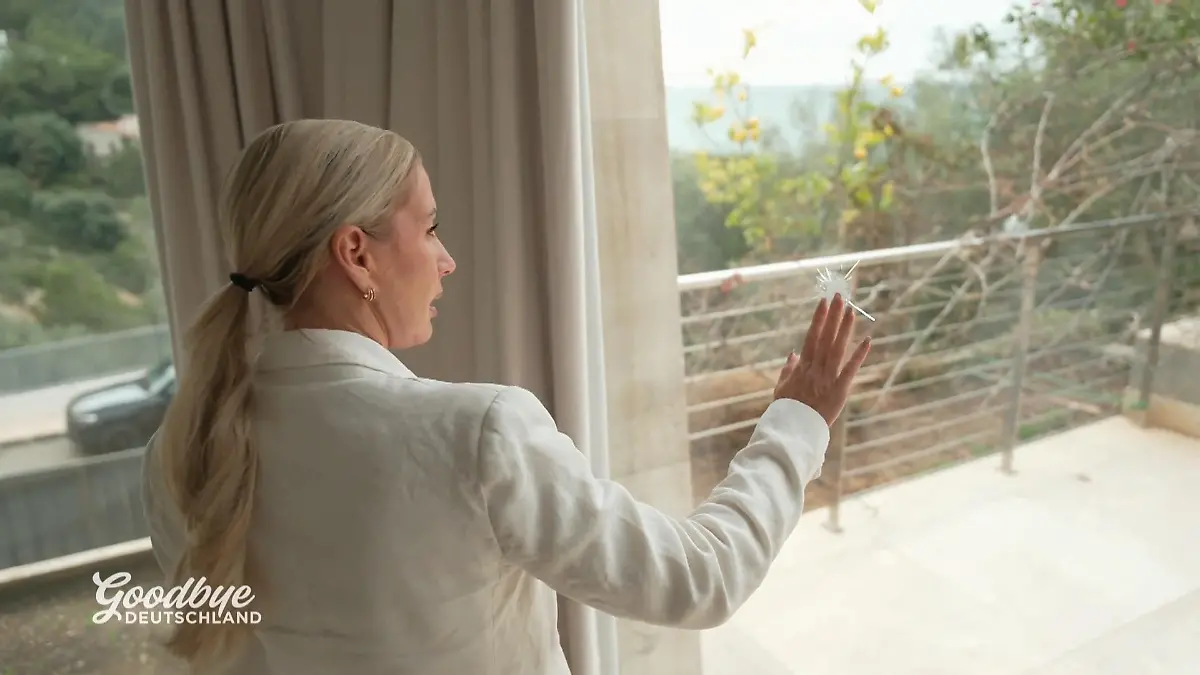 Peggy berührt mit der Hand eine Einschussstelle in einem Fenster. 