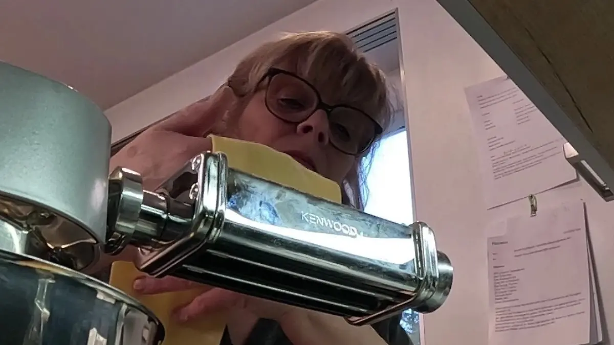 Froschperspektive auf Annett, die eine Teigbahn durch ihre Küchenmaschine führt. 