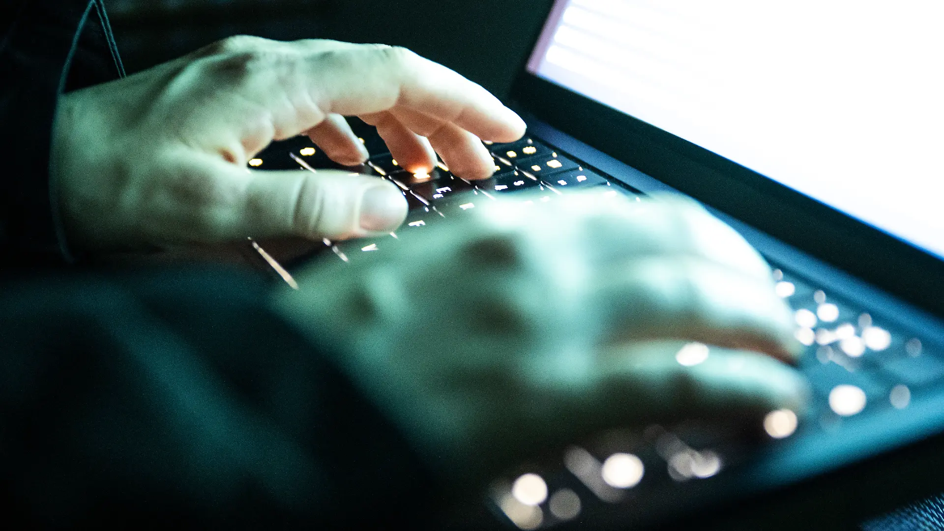 Eine Person tippt mit den Fingern auf einer beleuchteten Laptop-Tastatur.(gestellte Szene)