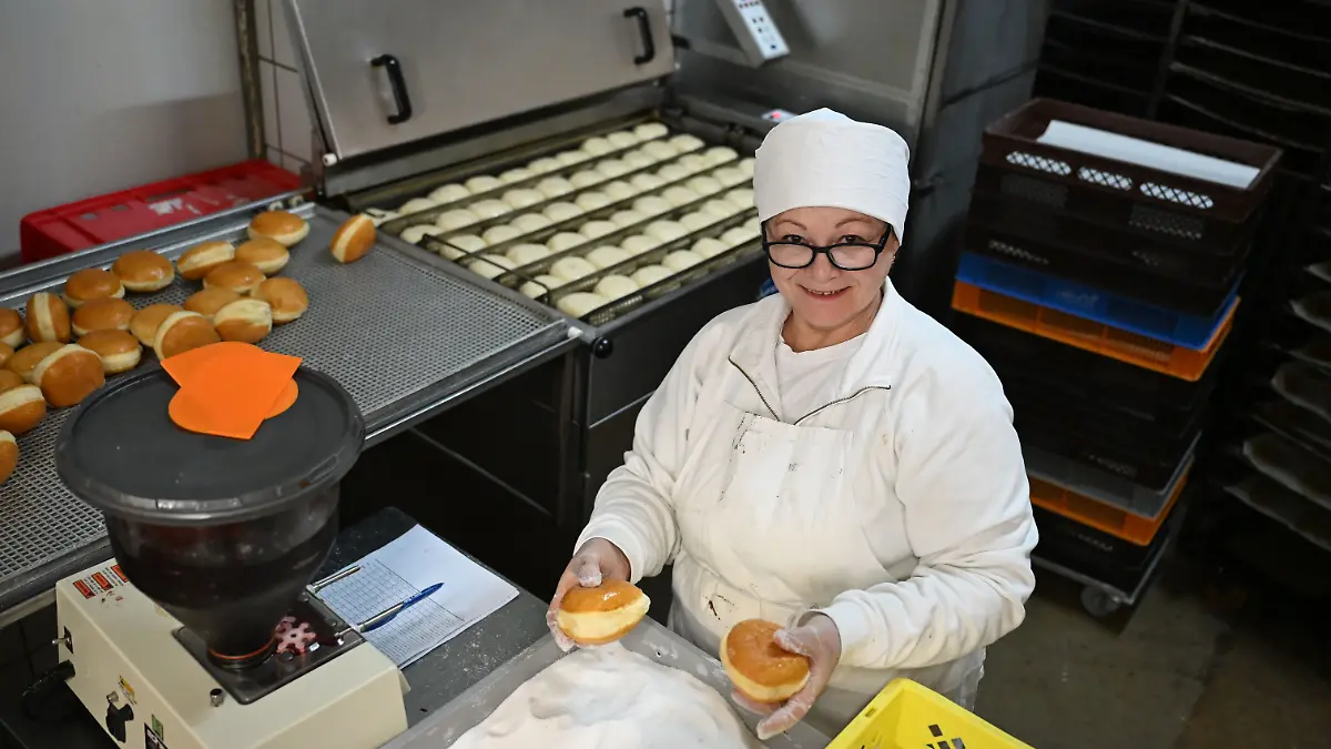 PRODUKTION - 11.12.2025, Hessen, Nidderau-Windecken: Bäckerin Svitlana Liashenko bepudert Berliner mit Zucker. Sie ist aus der Ukraine geflohen. (zu dpa: «Migranten schließen Lücken in Hessens Bäckereien») Foto: Michael Brandt/dpa +++ dpa-Bildfunk +++