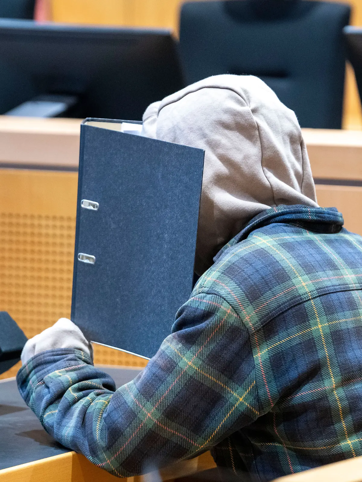  Im Schwurgerichtssaal des Landgerichts verbirgt sich ein Mann hinter einem Aktenordner. Der Angeklagte soll eine Frau im vergangenen Jahr mit vier Kopfschüssen umgebracht haben.