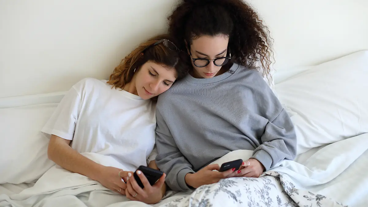 Zwei Frauen checken ihr Handy, eine hat ihren Kopf auf die Schulter der anderen gelegt.
