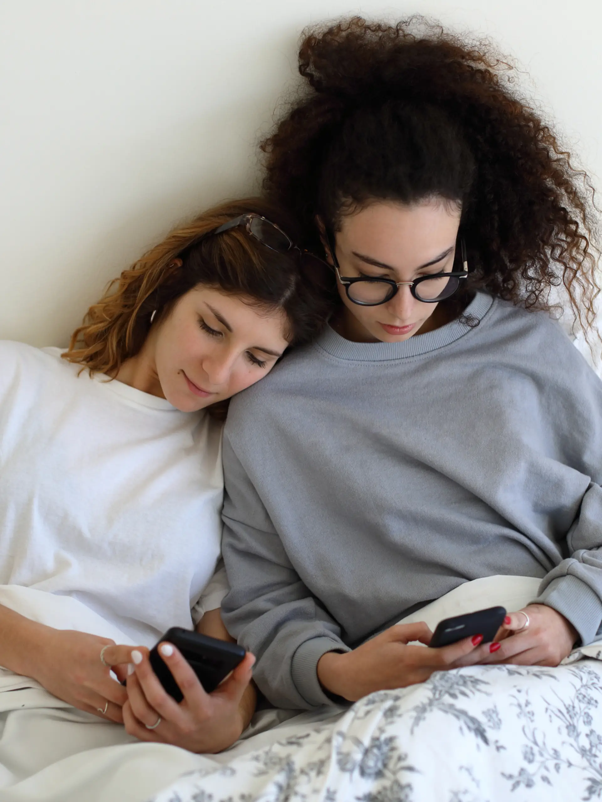 Zwei Frauen checken ihr Handy, eine hat ihren Kopf auf die Schulter der anderen gelegt.