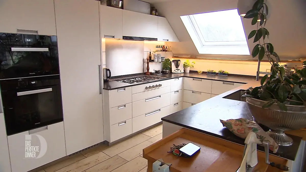 Das perfekte Dinner: Moderne große Küche mit cremefarbenen Fronten und schwarzer Arbeitsplatte unter einem Dachfenster