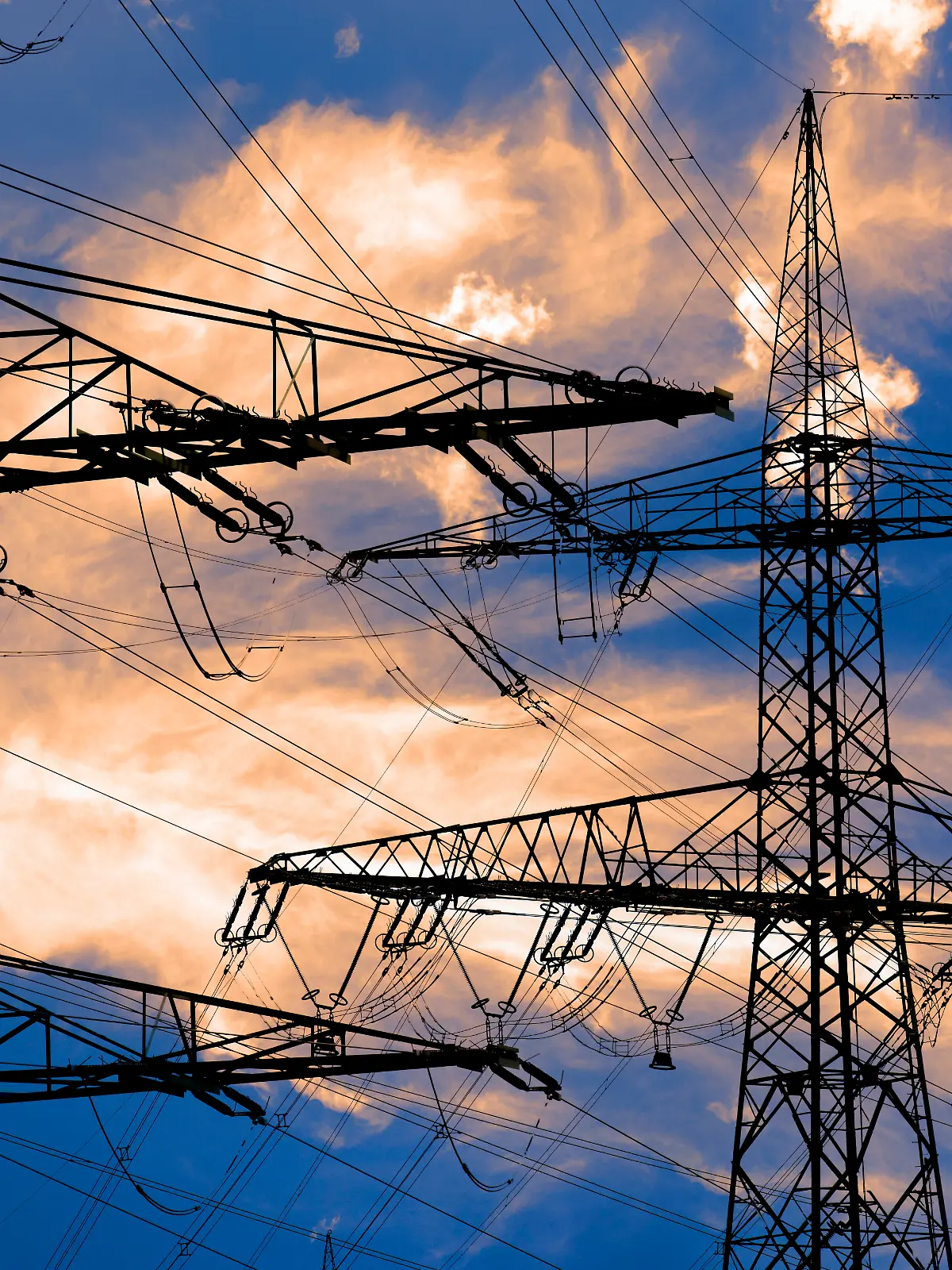 Hochspannungsmasten stehen vor einem Himmel mit dramatischen Wolken als Symbolbild für die Infrastruktur der Energieversorgung durch Elektrizität - FOTOMONTAGE