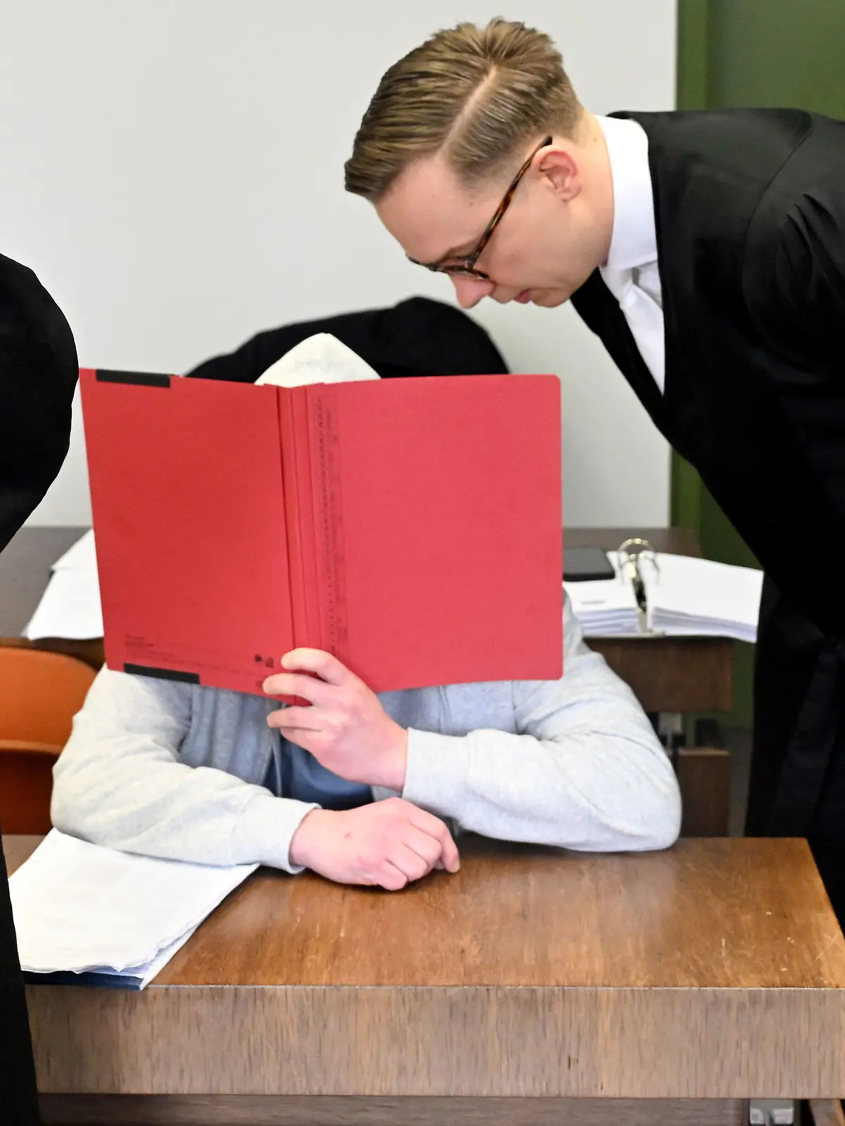 ARCHIV - 18.02.2026, Bayern, München: Der Angeklagte sitzt mit einem Ordner vor dem Gesicht vor Beginn des Prozess wegen Mordes an seiner Großmutter im Gerichtssaal im Landgericht München. Der Mann soll vor knapp einem Jahr seine Großmutter aus Habgier getötet haben. Die Großmutter hatte ihn stets unterstützt, auch finanziell. Als sie mit Kontaktabbruch drohte, soll er sie getötet haben. (zu dpa: «Enkel wegen Mordes an seiner Großmutter verurteilt»)