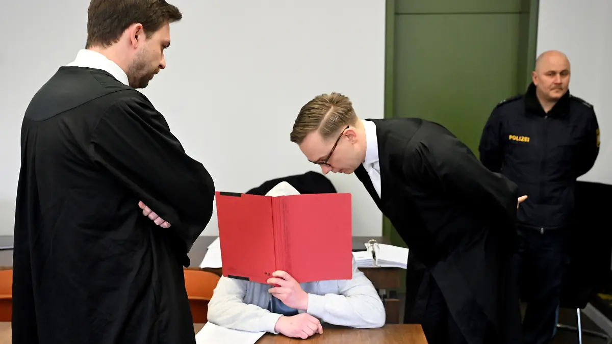 ARCHIV - 18.02.2026, Bayern, München: Der Angeklagte sitzt mit einem Ordner vor dem Gesicht vor Beginn des Prozess wegen Mordes an seiner Großmutter im Gerichtssaal im Landgericht München. Der Mann soll vor knapp einem Jahr seine Großmutter aus Habgier getötet haben. Die Großmutter hatte ihn stets unterstützt, auch finanziell. Als sie mit Kontaktabbruch drohte, soll er sie getötet haben. (zu dpa: «Enkel wegen Mordes an seiner Großmutter verurteilt»)