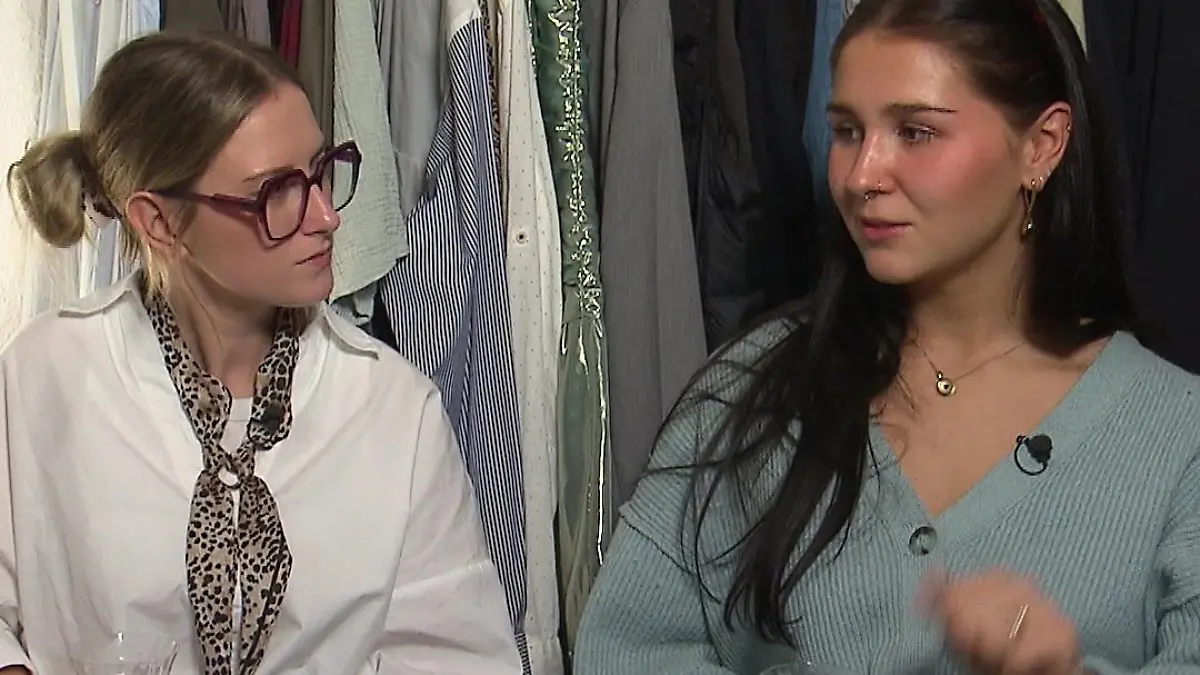 Luna und Antonia sitzen mit einem Glas Weißwein in der Hand vor einem Kleiderständer