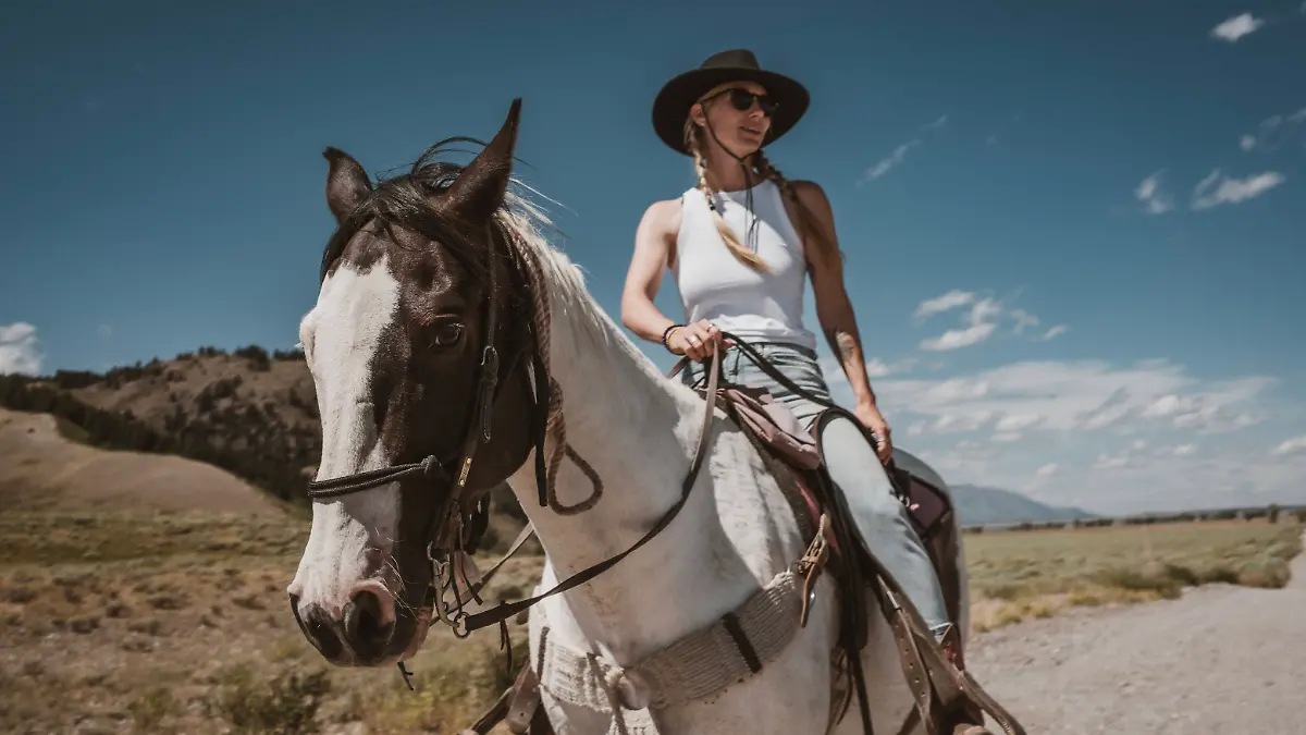 Frau mit Cowboy-Hut und Boots reitet auf einem Pferd.