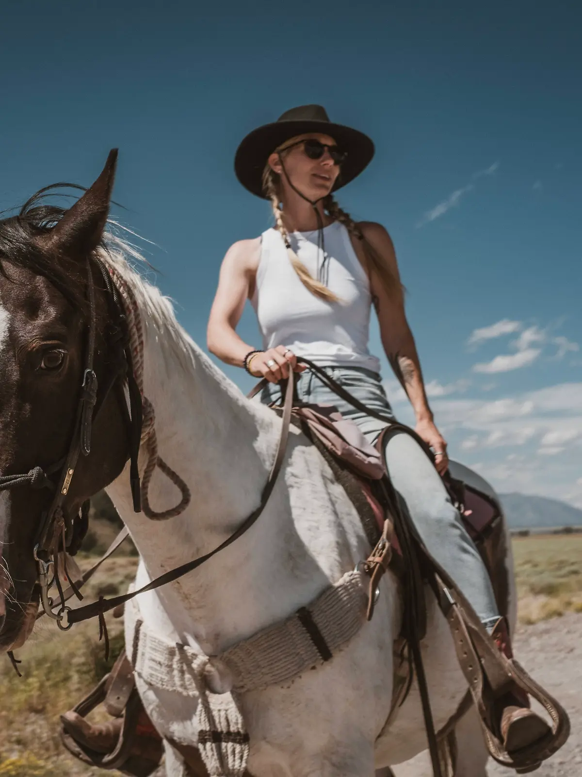 Frau mit Cowboy-Hut und Boots reitet auf einem Pferd.